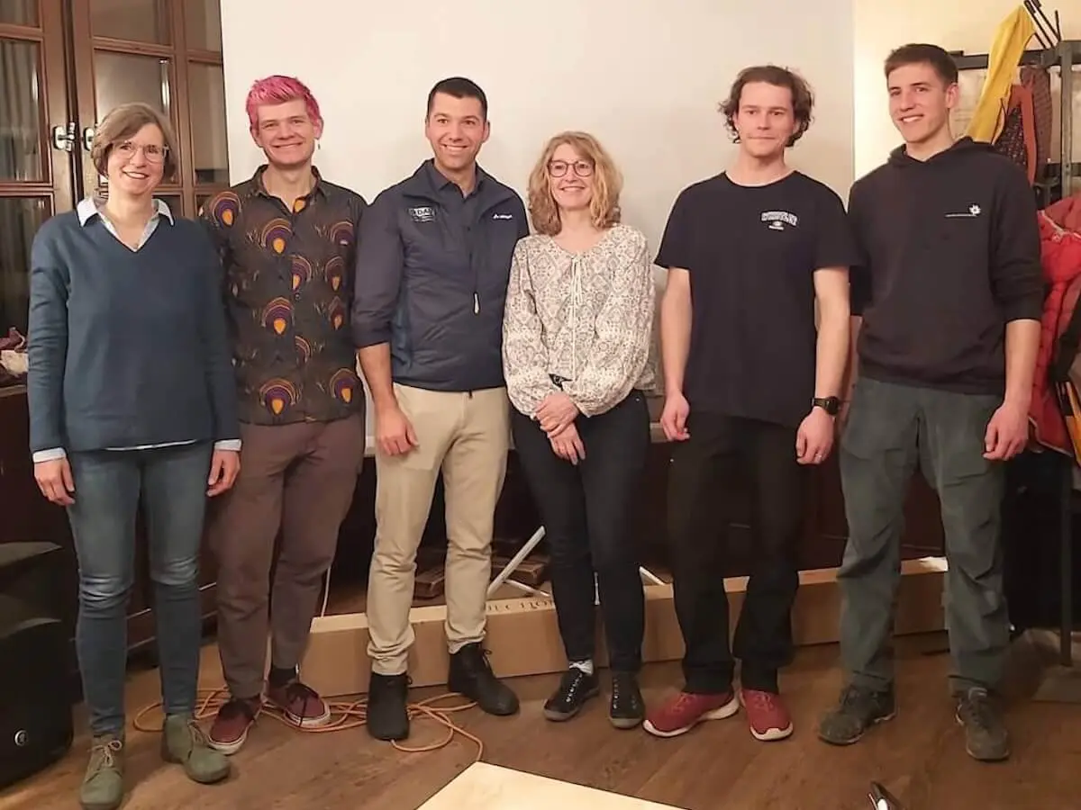 Sechs Personen, der neu gewählte Vorstand, stehen in einem Raum mit einer Leinwand und Holzfußboden. | © DAV Markt Schwaben/Martina Straub