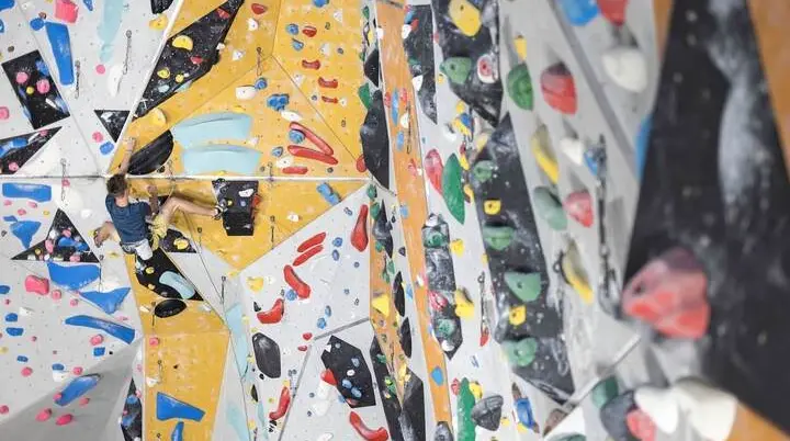Bunte Griffe und Routen in einer Kletterhalle - in der Entfernung sieht man einen Sportler | © DAV / Jens Klatt